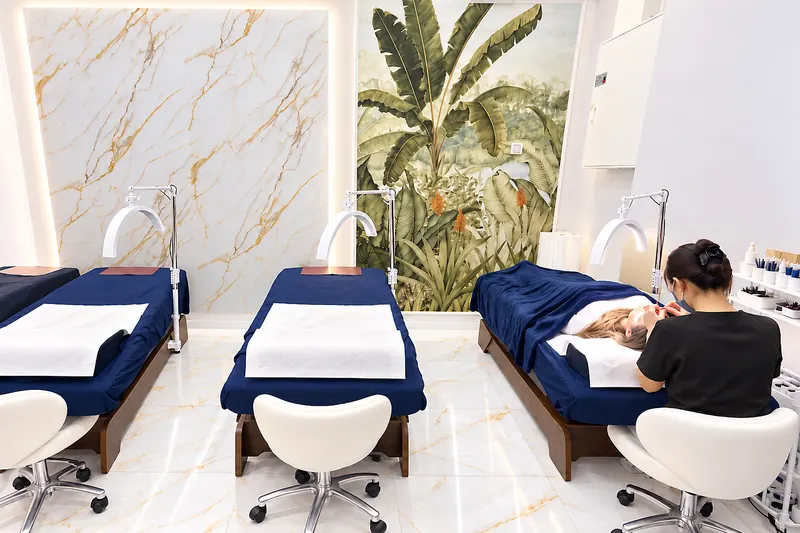 Wimpernbereich mit drei Liegen vor Marmorwand und Pflanzentapete